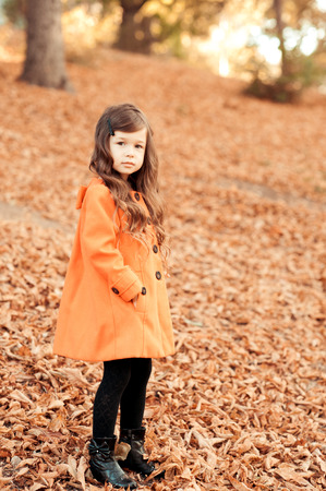 Kid girl 4-5 year old wearing stylish coat and knitted hat in park. Standing outdoors. Looking at camera. Childhood.の写真素材
