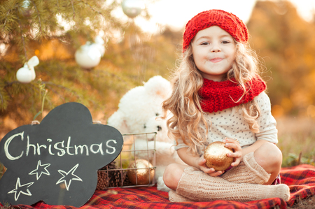Funny kid girl 4-5 year old holding christmas decorations outdoors. Smiling child. Celebration. Looking at camera.の写真素材
