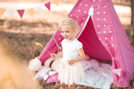 Smiling baby girl wearing white skirt and summer top playing outdoors with wigwam. Birthday party. Childhood.の写真素材