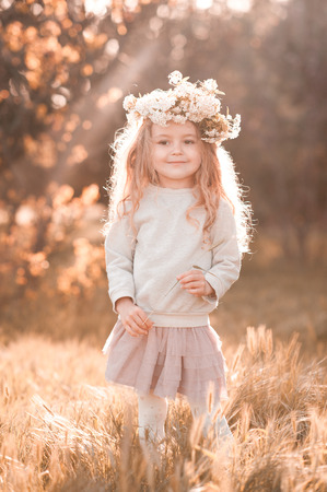 Cute baby girl 4-5 year old walking in park wearing flower wreath. Looking at camera. Childhood. の写真素材