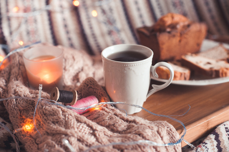 Cup of black tea with cake and candle staying on wooden tray in bed on knitted cloth closeup. Selective focus.の写真素材