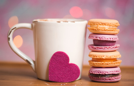 Cup of coffee with macaroons cookies and pink heart on wooden table over christmas lights. Selective focus.の写真素材