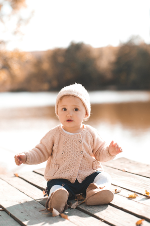 Cute baby girl 1 year old wearing stylish knitted clothes posing in autumn park outdoors. Looking at camera. の写真素材