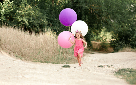 Stylish girl 4-5 year old running in park holding big balloonsの写真素材