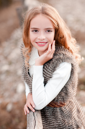 Smiling blonde kid girl 13-14 year old wearing fur vest and white sweater outdoors. Autumn season. Childhood.の写真素材