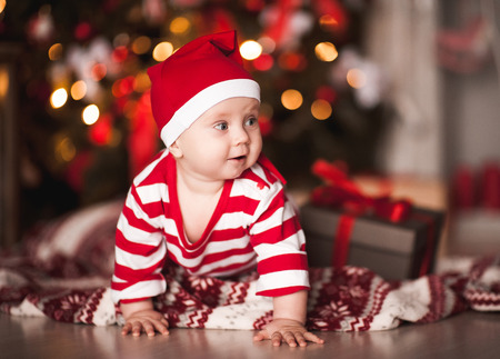 Cute infant girl wearing santa claus suit and hat crawling over Christmas lights. Merry Christmas. Holiday season. の写真素材