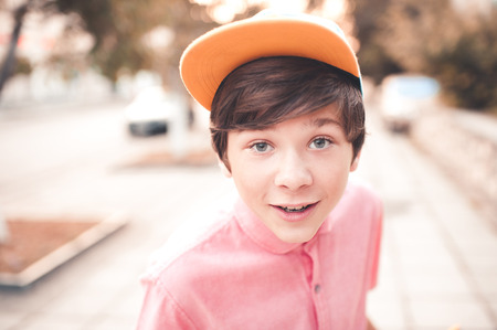 Stylish teen boy wearing cap and pink shirt outdoors. Having fun over city background. Looking at camera. Summer portrait of teenager closeup.の写真素材