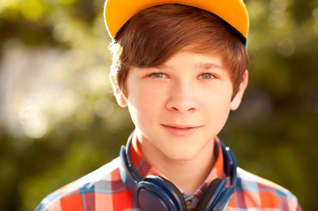 Smiling teen boy wearing stylish shirt and cap outdoors. Listening to musicの写真素材