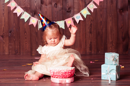 Baby girl 1 year old celebrating first birthday in room. Sitting on wooden floor eating cake. の写真素材