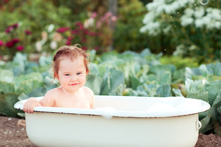 Smiling baby girl sitting in bath. Washing outdoors. Playing. Childhood.の写真素材