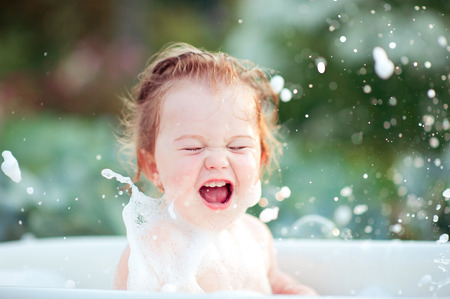 Laughing baby girl having fun washing in bath outdoors. Cheerful. Happiness. Childhood. の写真素材