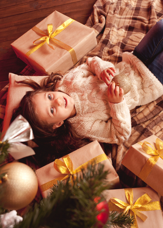 Cute girl 4-5 year old lying under christmas tree with many presents in room. Looking at camera. Top view.の写真素材
