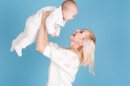 Happy woman having fun with her newborn child over blue. Wearing winter knitted clothes