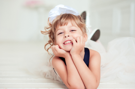 Smiling cute kid girl 4-5 year old lying on white wooden floor in room. Looking at camera. Childhood. の写真素材