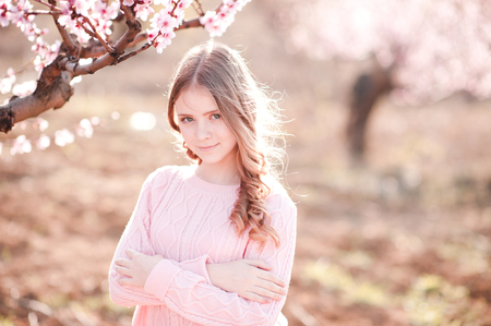 Smiling teen girl 14-16 year old posing in peach garden outdoors. Looking at camera. Teenager hood. の写真素材