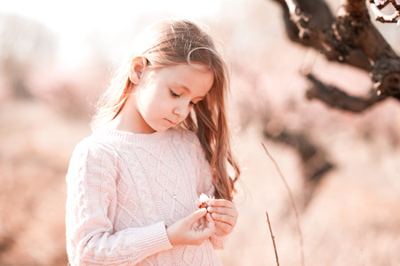 Cute baby girl 4-5 year old holding peach flower in meadow outdoors. Countryside. の写真素材