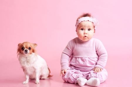Baby girl sitting on floor with little dog over pink. Wearing stylish clothes. Looking at camera. Childhood.の写真素材