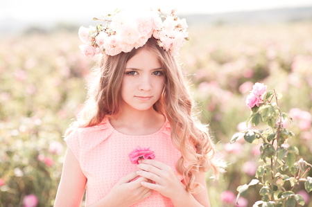 Blonde teen girl wearing wreath with roses outdoors. Holding flower. Looking at camera. Romance.の写真素材