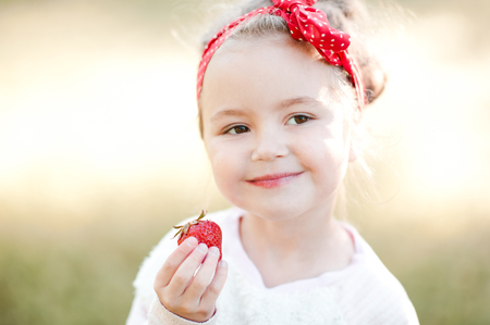 Smiling baby girl 4-5 year old eating fresh strawberry outdoors. Summer season. Childhood. の写真素材