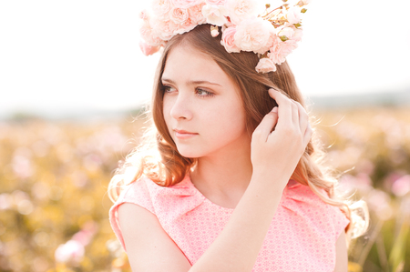 Summer portrait of teen girl 14-16 year old wearing floral wreath with roses outdoors. Standing in rose field. Looking away. の写真素材