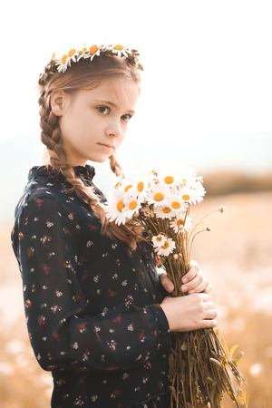 Stylish teenage girl 12-14 year old holding chamomile flowers outdoors in field. Looking away. Childhood. の写真素材