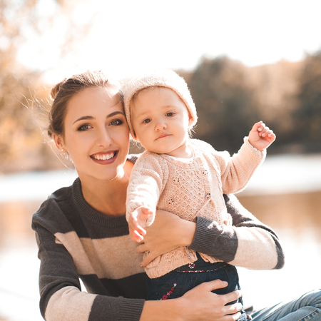 Smiling mother holding baby girl 1 year old wearing knitted clothes posing outdoors. Looking at camera. Motherhood. の写真素材