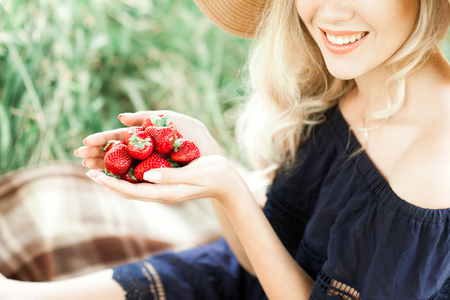 Smiling girl holding strawberry in hands close up outdoors. Healthy eating. の写真素材