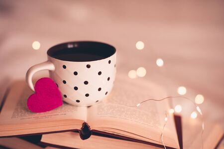 Cup of coffee with pink heart on open books close up. Winter holiday season. Valentines Day. Good morning. の写真素材