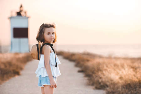 Smiling child girl 4-5 year old wearing big black hat and white top posing over blue sea background close up. Looking at camera. Summer travel season.の写真素材