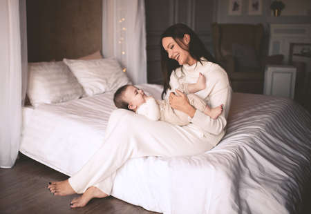 Young mother kissing baby boy in room closeup. Having fun indoors. Childhood. Happiness.