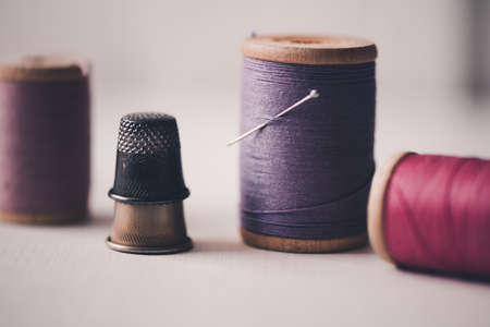 Stackof thimbles with spool of thread staying on table closeup. Handmade.