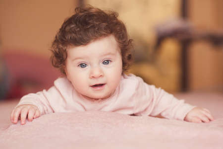 Happy baby with curly hair lying in bed holding mother hands cloeup. Top view. Motherhood....