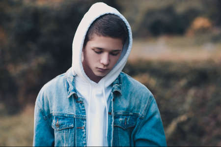 Handsome blond teen boy 16-17 year old wearing hoodie and denim jacket outdoors. Looking at camera. Spring season.の写真素材