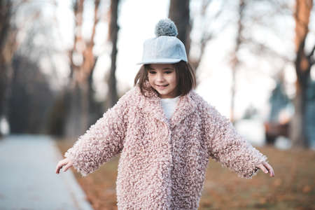 Pretty child girl 3-4 year old wearing stylish autumn clothes posing in street over city background closeup. Looking at camera. Childhood.の写真素材