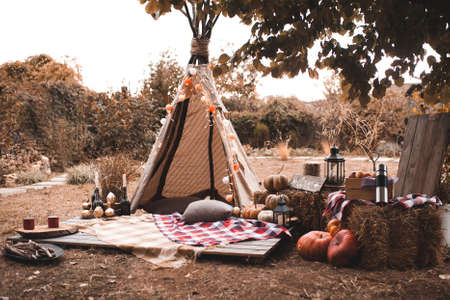 Stylish wigwam with lights, pumpkins and stack of hay outdoors. Autumn season.の写真素材