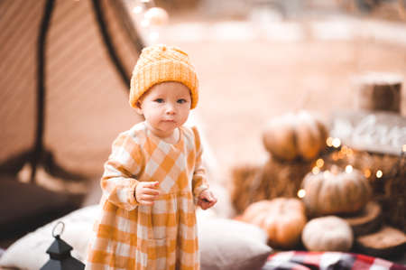 Cute baby girl 1-2 year old wearing yellow knitted hat and dress over lights at background.の写真素材