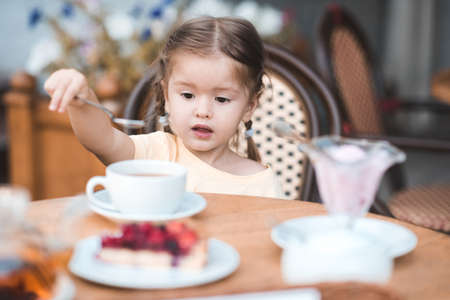 Cute baby girl 1-2 year old eating fruit cake and drinking tea in cafe outdoors. Childhood.の写真素材