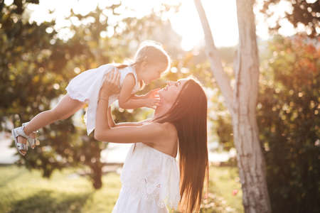 Mother holding baby girl having fun in sun light over nature background. Motherhood. Childhood.の写真素材