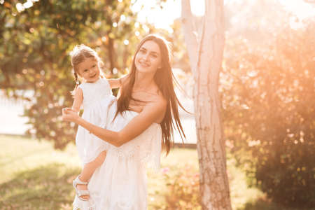 Funny baby girl 2-3 year old sitting on mother hands in sun light over nature background. Motherhood. Childhood.の写真素材