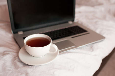 Cup of black tea on laptop in bed closeup. Quarantine time. Working at home. Good morning.