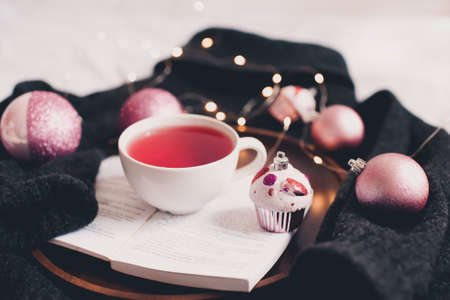 Fresh hot morning cup of tea on open book with Christmas decorations on knitted sweater over Christmas glowing lights at background close up. Good morning. Winter holiday season.の写真素材