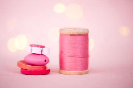 Stack of colorful buttons with pink cotton thread over lights at background. Selective focus.