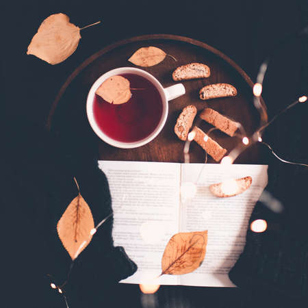 Cup of tea with fallen leaves and open book staying on knitted sweater closeup. Top view. Good morning.の写真素材