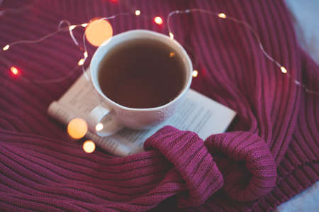 Cup of fresh tea staying on open book and knitted sweater closeup. Good morning. Christmas season.の写真素材