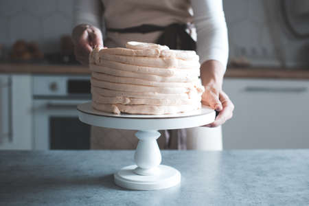 Woman decorating tasty cake with whipped cream on tray standing in kitchen closeup. Wedding day. Birthday party.の写真素材