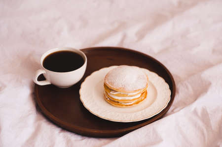 Fresh morning cup of coffee with pancakes on wooden tray in bed closeup. Good morning. Selective focus.の写真素材
