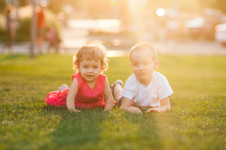 Two cheerful little kids having fun lying on bright green grass over sun light background closeup. Childhood. Summer season. Happiness.の写真素材
