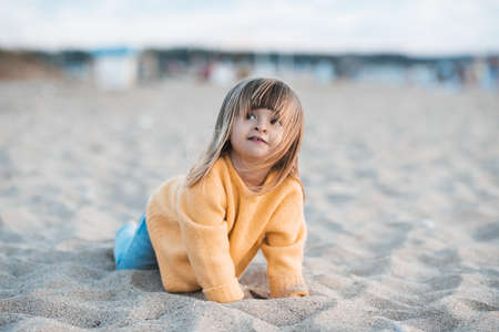 Cute kid girl 2-3 year old wearing knitted yellow sweater and denim pants having fun at beach playing with sand outdoors closeup. Childhood. Autumn season.の写真素材