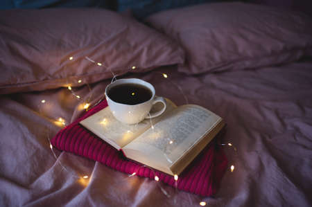 Open book with lights and tasty cup of tea in bed close up. Good morning. Selective focus. Winter holiday season.の写真素材