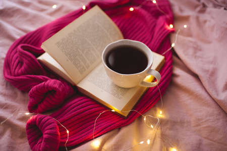 Tasty cup of tea with knitte cloth and open book in bed. Good morning. Selective focus.の写真素材